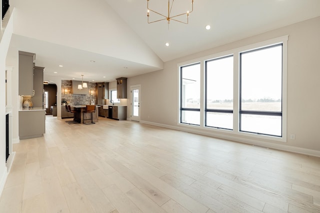 unfurnished living room with arched walkways, high vaulted ceiling, recessed lighting, light wood-style floors, and an inviting chandelier