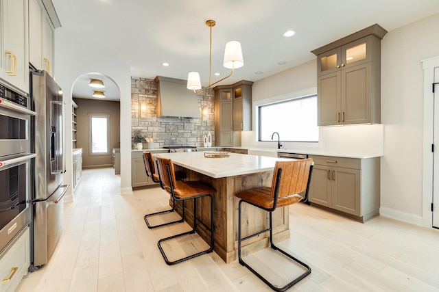 kitchen with glass insert cabinets, a center island, hanging light fixtures, light countertops, and premium range hood