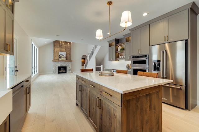 kitchen featuring lofted ceiling, a kitchen island, stainless steel appliances, a fireplace, and pendant lighting