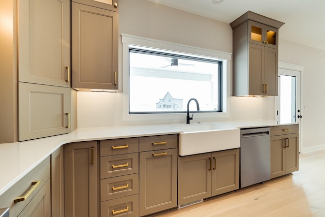 kitchen with a sink, glass insert cabinets, light countertops, and dishwasher