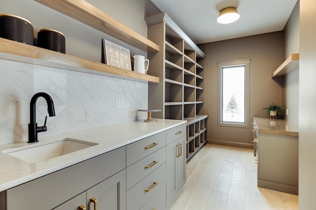 kitchen with decorative backsplash, light wood-style flooring, light stone countertops, open shelves, and a sink