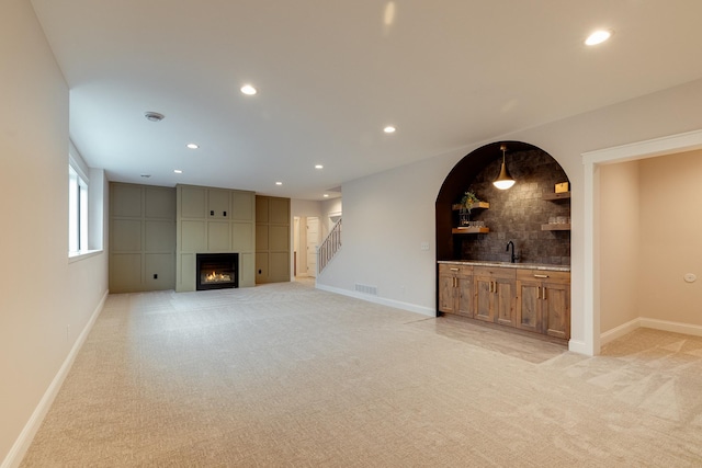 unfurnished living room with a large fireplace, a sink, visible vents, and light colored carpet