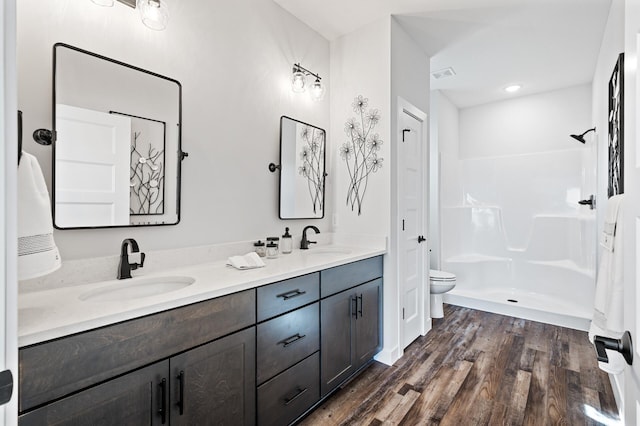 bathroom featuring a shower, hardwood / wood-style floors, double sink, vanity with extensive cabinet space, and toilet