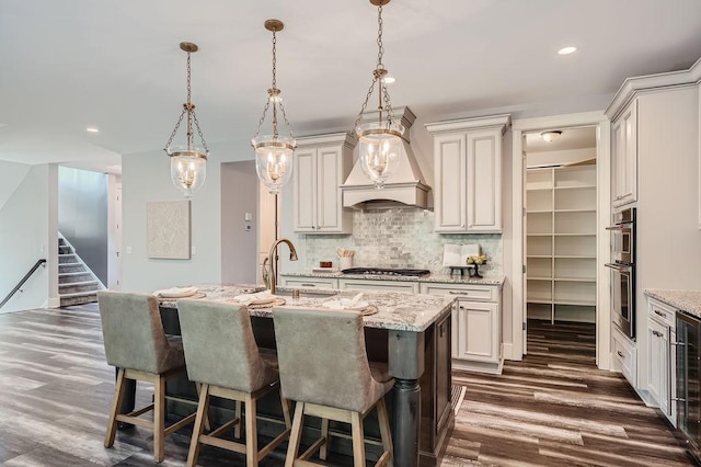 kitchen with a center island with sink, custom exhaust hood, pendant lighting, and decorative backsplash