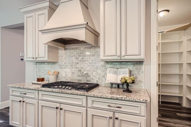 kitchen featuring stainless steel gas cooktop, premium range hood, dark wood-type flooring, backsplash, and light stone countertops