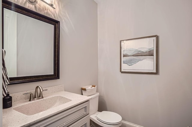 half bathroom with baseboards, vanity, and toilet