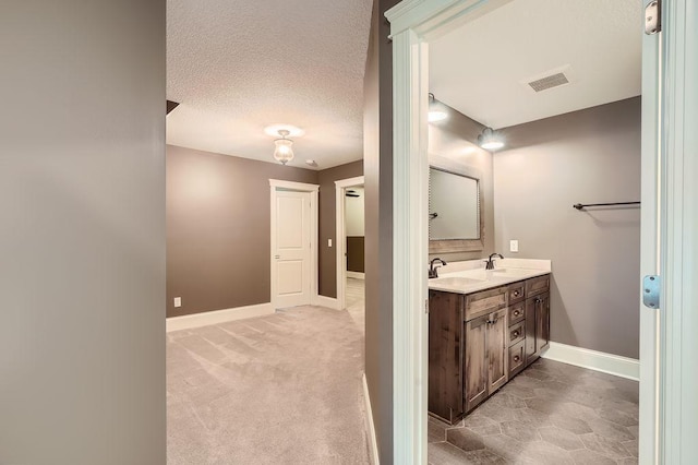 bathroom with a textured ceiling, a sink, visible vents, baseboards, and double vanity