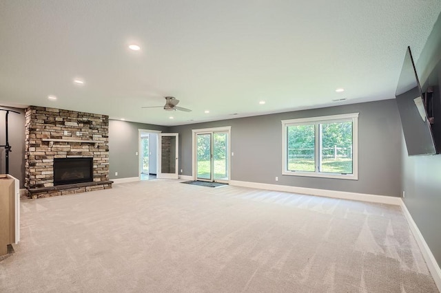 unfurnished living room with recessed lighting, baseboards, a stone fireplace, and light colored carpet