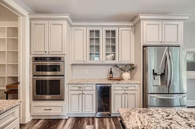 kitchen with appliances with stainless steel finishes, beverage cooler, glass insert cabinets, and light stone counters