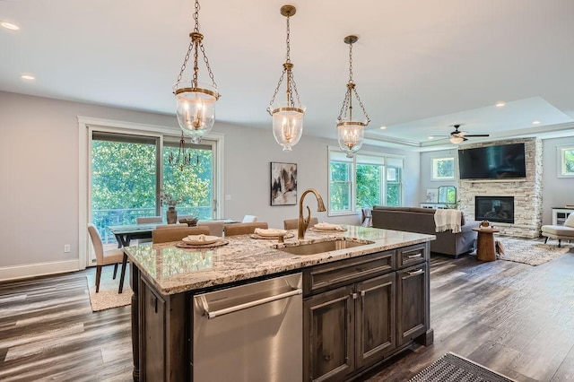 kitchen featuring decorative light fixtures, stainless steel dishwasher, a kitchen island with sink, a sink, and light stone countertops