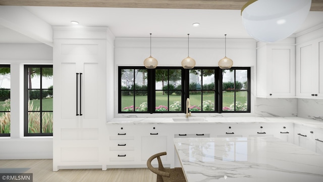 kitchen with sink, white cabinets, hanging light fixtures, light stone counters, and plenty of natural light