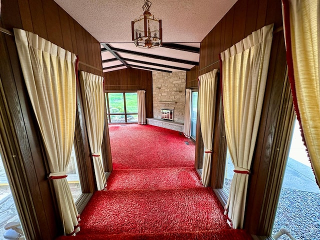 hallway with a textured ceiling, carpet, vaulted ceiling with beams, and wood walls