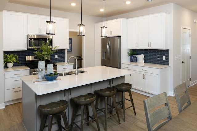 kitchen featuring white cabinets, appliances with stainless steel finishes, a kitchen island with sink, and sink