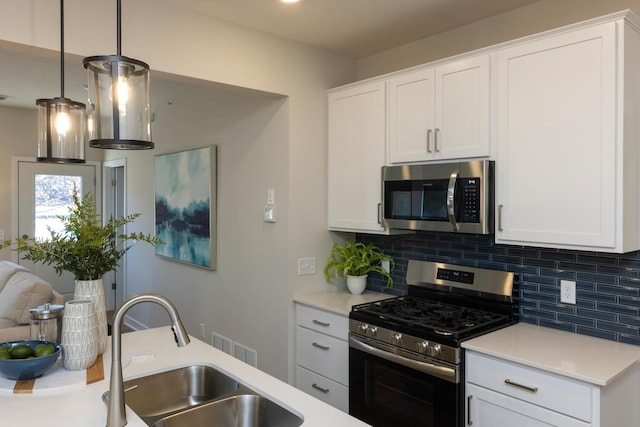 kitchen featuring backsplash, white cabinets, pendant lighting, and appliances with stainless steel finishes