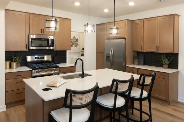 kitchen featuring light hardwood / wood-style flooring, appliances with stainless steel finishes, a kitchen island with sink, sink, and tasteful backsplash