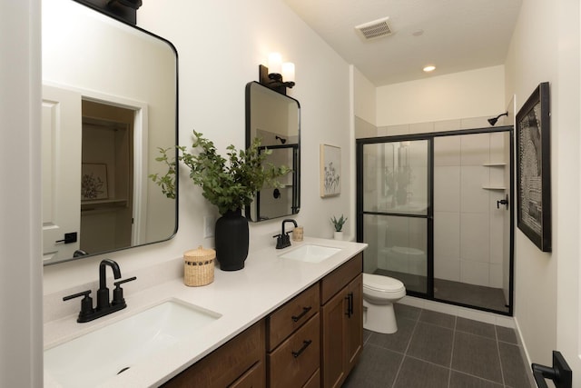 bathroom featuring a shower with shower door, dual vanity, tile flooring, and toilet