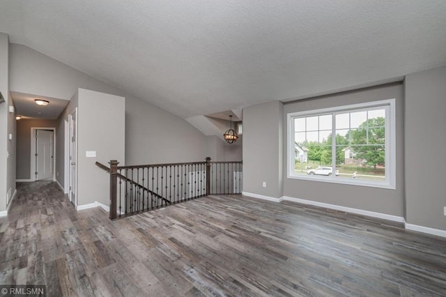 spare room featuring a textured ceiling, dark hardwood / wood-style floors, vaulted ceiling, and a notable chandelier