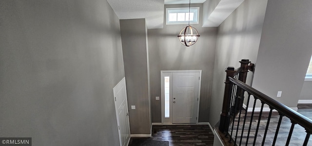 foyer featuring a towering ceiling, dark wood-type flooring, a textured ceiling, and an inviting chandelier