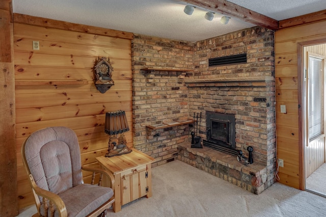 sitting room featuring a textured ceiling, light carpet, a brick fireplace, and beam ceiling