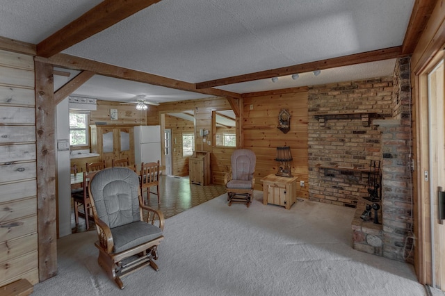 living area featuring wooden walls, a textured ceiling, carpet flooring, beam ceiling, and ceiling fan