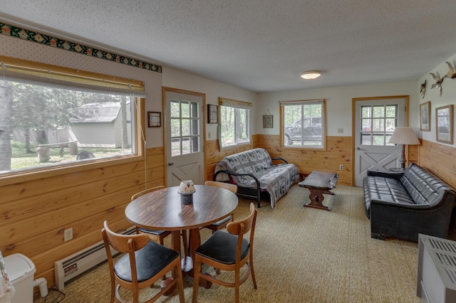 carpeted dining space with wood walls, a textured ceiling, and a baseboard heating unit