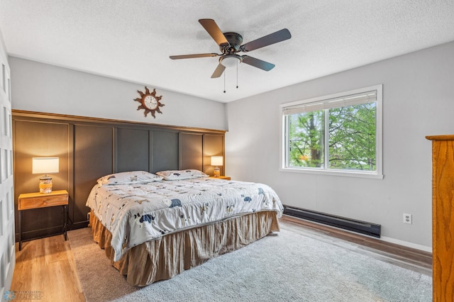 bedroom featuring ceiling fan, light hardwood / wood-style floors, a textured ceiling, and a baseboard heating unit