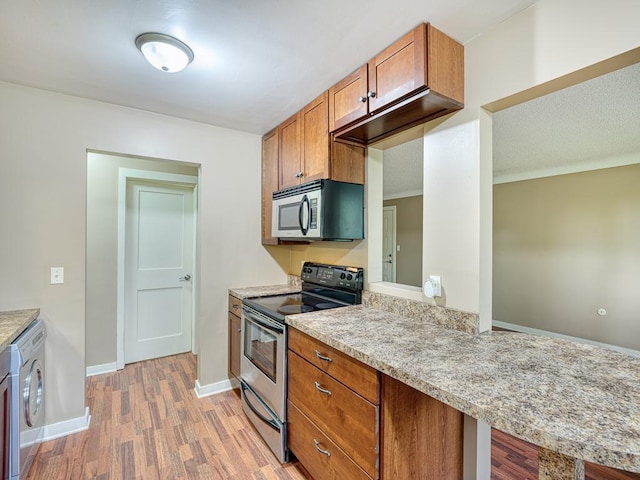 kitchen with light stone countertops, washer / dryer, light wood-type flooring, and appliances with stainless steel finishes