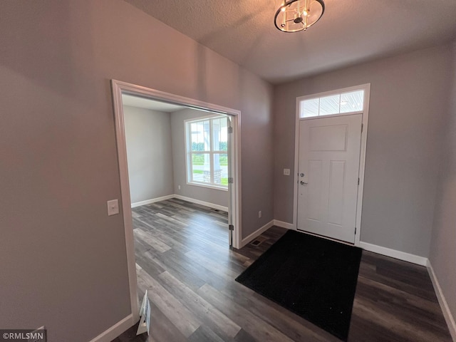 entrance foyer featuring a textured ceiling, a notable chandelier, dark hardwood / wood-style floors, and plenty of natural light