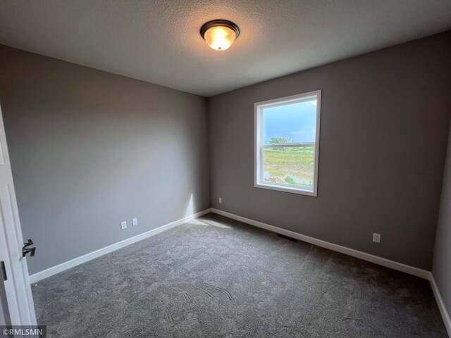 empty room with dark colored carpet and a textured ceiling