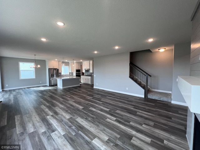 unfurnished living room with a textured ceiling, dark hardwood / wood-style floors, and a chandelier