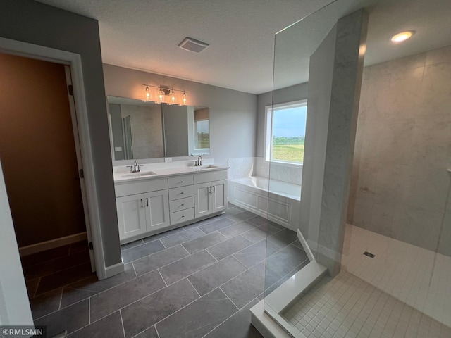 bathroom with a textured ceiling, vanity, plus walk in shower, and tile patterned floors