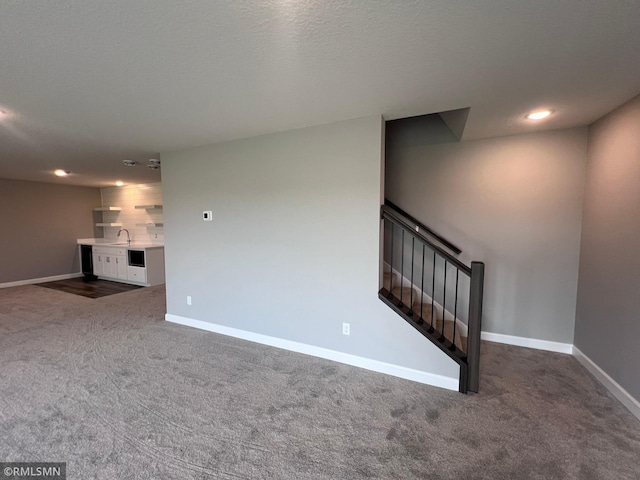 unfurnished living room with a textured ceiling, dark colored carpet, and sink