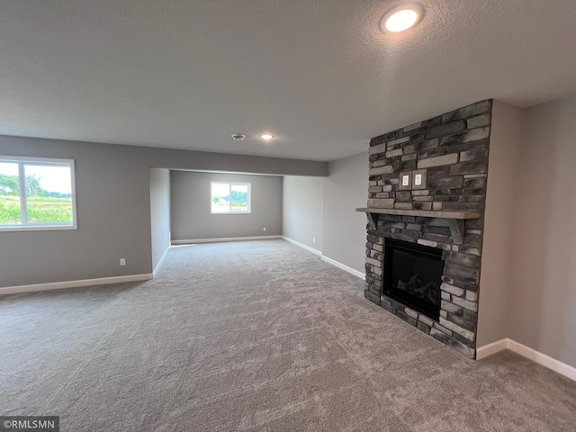 unfurnished living room with a stone fireplace, a textured ceiling, and carpet flooring