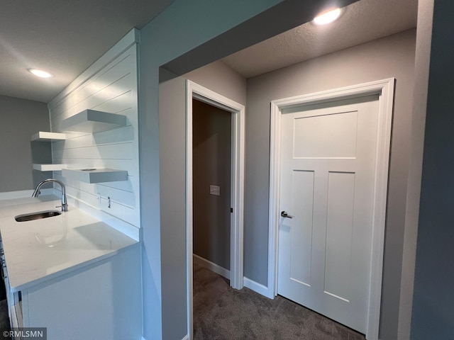 corridor with dark carpet, a textured ceiling, and sink