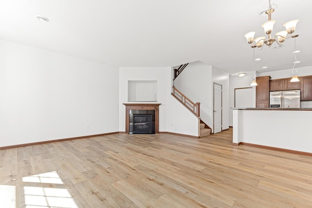 unfurnished living room with a tiled fireplace, an inviting chandelier, and light hardwood / wood-style floors