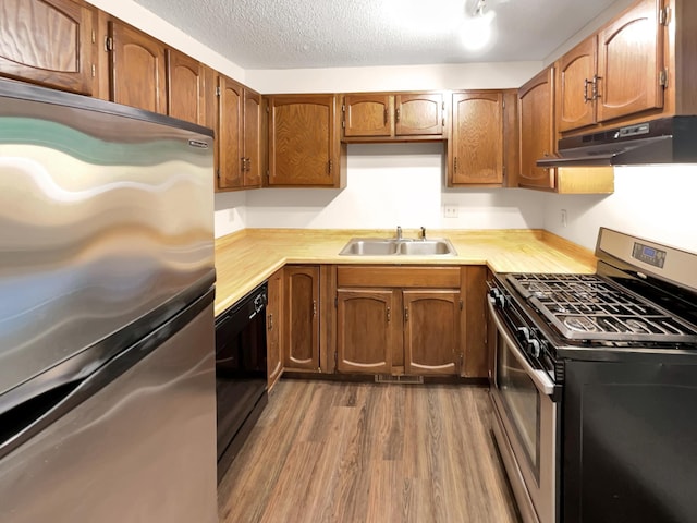 kitchen with stainless steel appliances, a textured ceiling, sink, and wood-type flooring