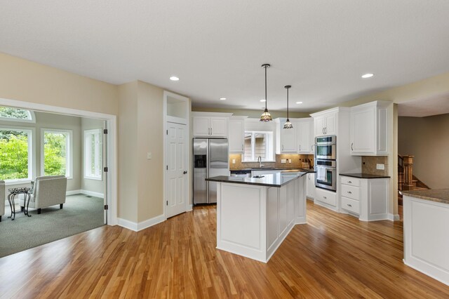 kitchen featuring white cabinets, stainless steel appliances, decorative light fixtures, and light hardwood / wood-style floors