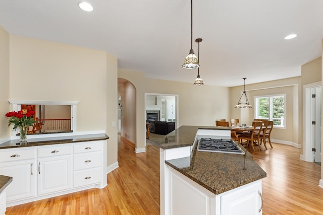 kitchen with stainless steel gas stovetop, dark stone counters, light hardwood / wood-style floors, decorative light fixtures, and white cabinets