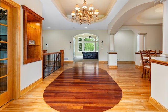 interior space featuring ceiling fan with notable chandelier, ornate columns, light wood-type flooring, and a tray ceiling