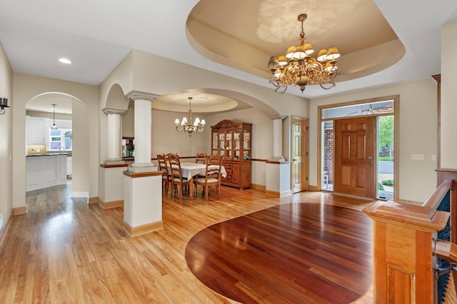 foyer with a chandelier, a raised ceiling, ornate columns, and light hardwood / wood-style flooring