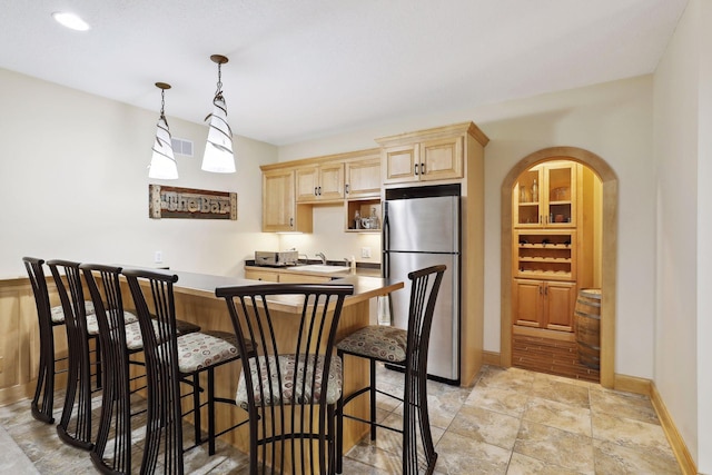 kitchen featuring a breakfast bar, stainless steel fridge, hanging light fixtures, and light brown cabinetry