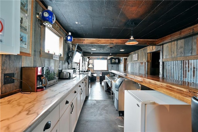 kitchen with a wealth of natural light, hanging light fixtures, white cabinetry, and concrete flooring