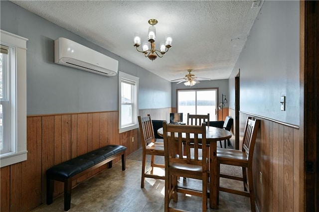 tiled dining space featuring an AC wall unit, ceiling fan with notable chandelier, and a textured ceiling