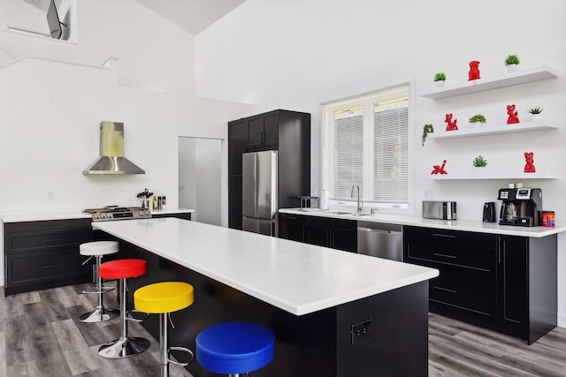 kitchen with light wood-type flooring, stainless steel appliances, wall chimney range hood, a center island, and a breakfast bar area