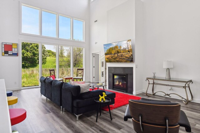 living room with plenty of natural light, a tile fireplace, wood-type flooring, and a towering ceiling