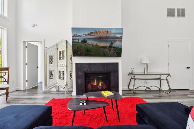 living room with a tile fireplace, a towering ceiling, and hardwood / wood-style flooring