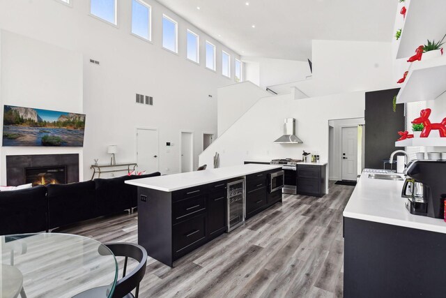 kitchen with a high ceiling, wall chimney range hood, sink, stainless steel stove, and wine cooler