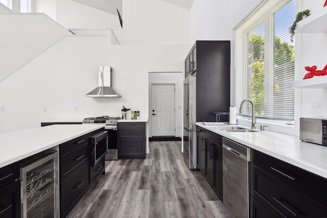 kitchen with a healthy amount of sunlight, wall chimney range hood, wine cooler, light hardwood / wood-style floors, and appliances with stainless steel finishes