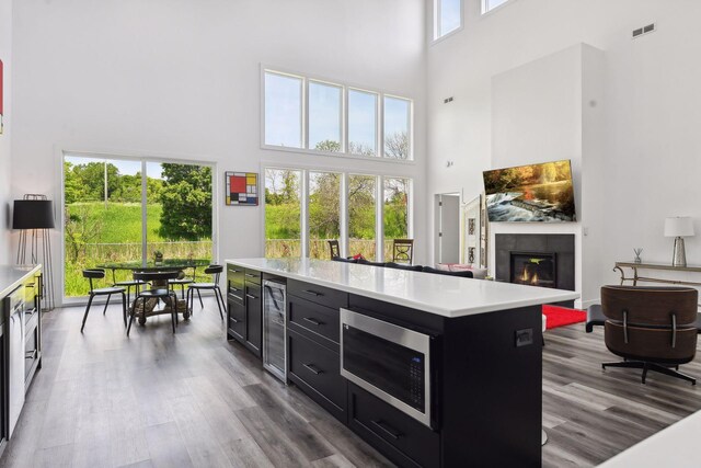 kitchen featuring stainless steel microwave, a center island, beverage cooler, a towering ceiling, and wood-type flooring