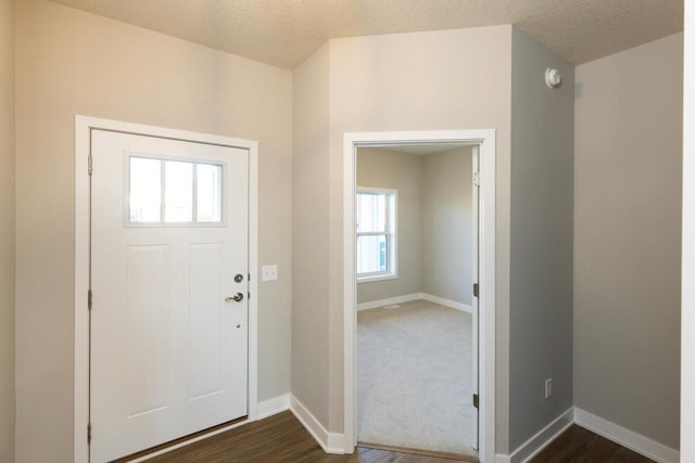 entryway featuring a healthy amount of sunlight, dark colored carpet, and a textured ceiling